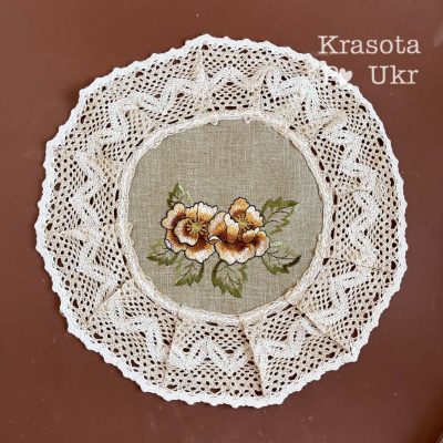 Кругла серветка з мереживними краями, прикрашена вишивкою шоколадно-коричневих квітів матіоли на світлому фоні.